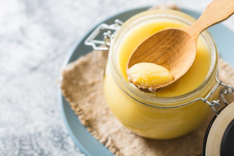 A jar of ghee with a spoon, on a cloth and a plate