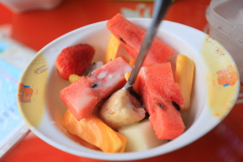 A white dish containing a fruit salad called hoa qua dam which uses condensed milk as an ingredient