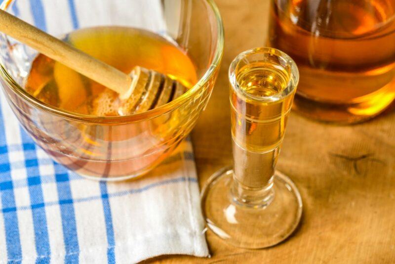 A glass jar of honey, next to a small glass of mead