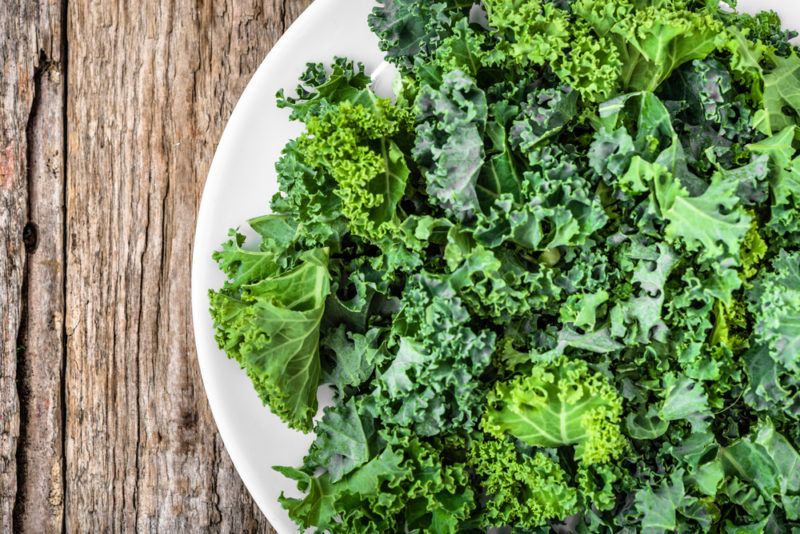 A white bowl or plate with curly kale on a wooden table