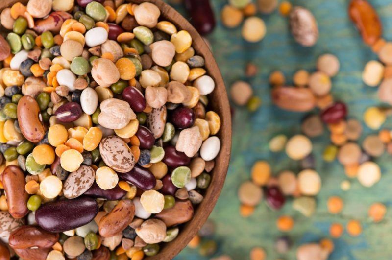 A large brown bowl of legumes, with some more scattered on the cloth beneath