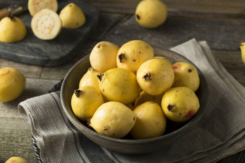 A gray dish containing a pile of lemon guava, with more guavas in the background