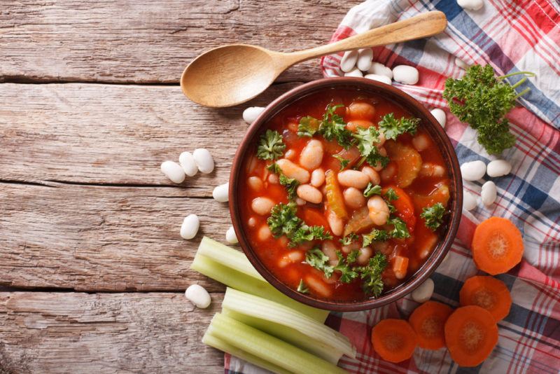 A brown bowl with minestrone soup and vegetables scattered around