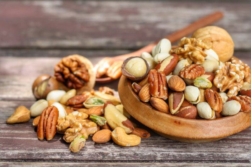 A bowl of mixed nuts with more of the nuts on the table