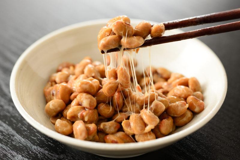 A bowl of natto soy beans with some being pulled out using chopsticks