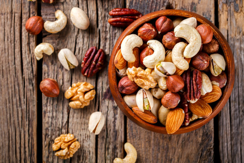 A brown bowl of nuts, with a handful or so more nuts scattered on the table