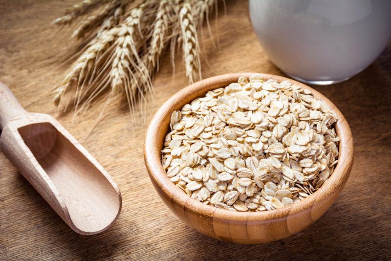 A brown bowl with oats, next to a scoop and some oats