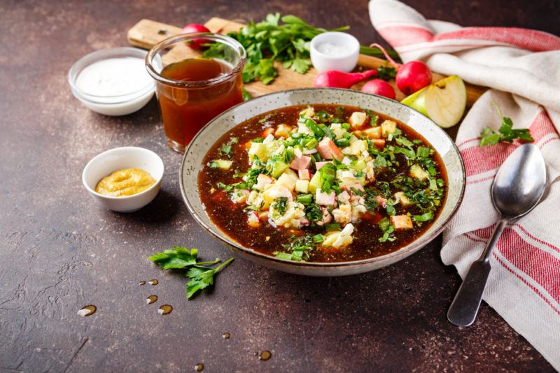 A bowl of okroshka soup on a table next to sauces