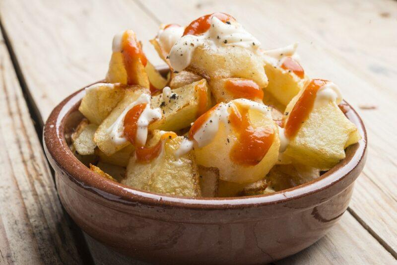 A brown bowl filled with patatas bravas, covered in a red sauce and a mayo-based one