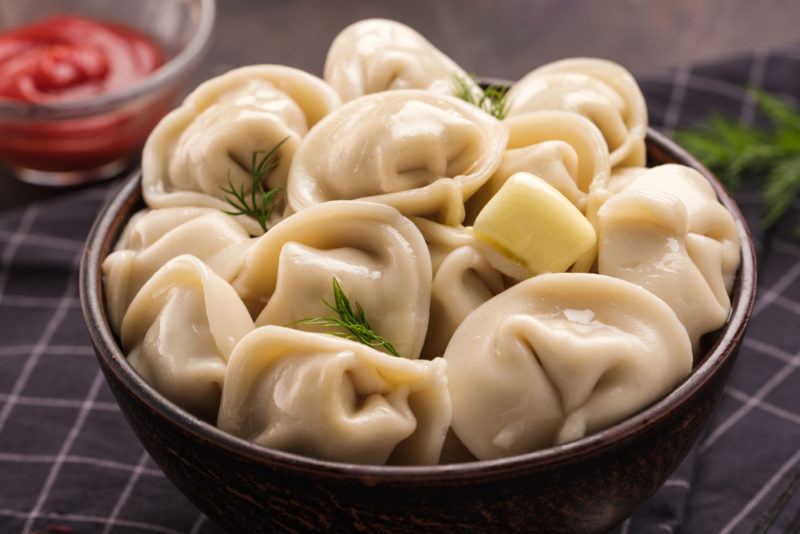 A brown bowl of pelmeni next to red sauce