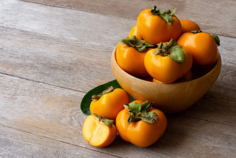 A brown bowl with Fuyu persimmons