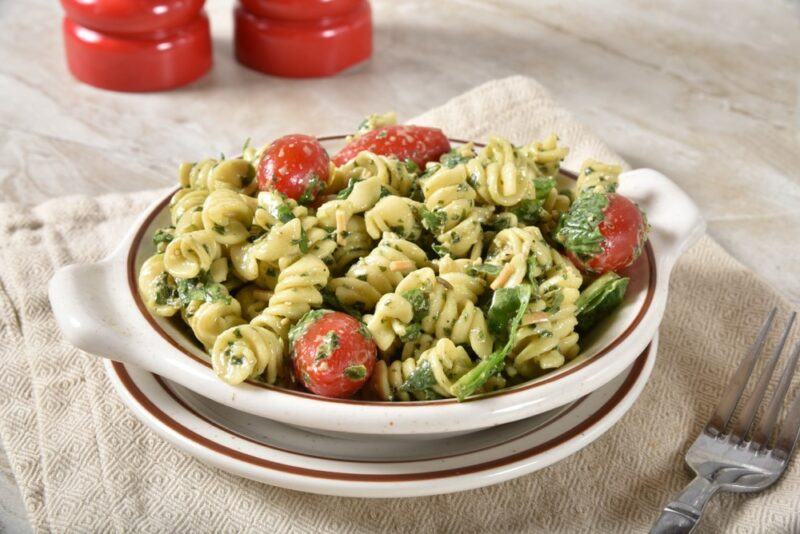 A large white dish containing a pesto pasta salad with cherry tomatoes