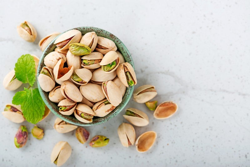 A marble table with a bowl of pistachio nuts and a few more scattered on the table