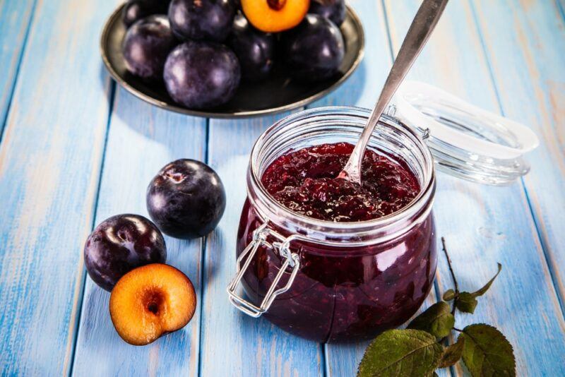 A light blue wooden table, with a few plums, a bowl of plums and some homemade plum jam