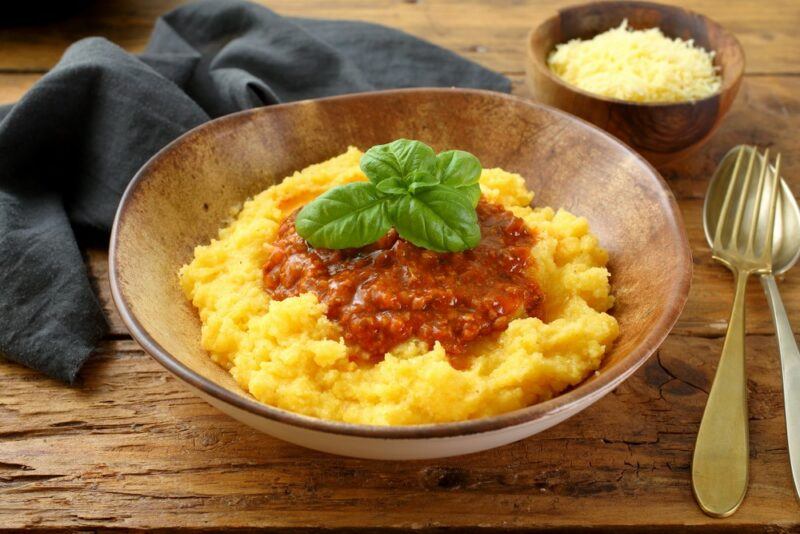 A wooden bowl with polenta with a ragu sauce, next to a fork and a spoon