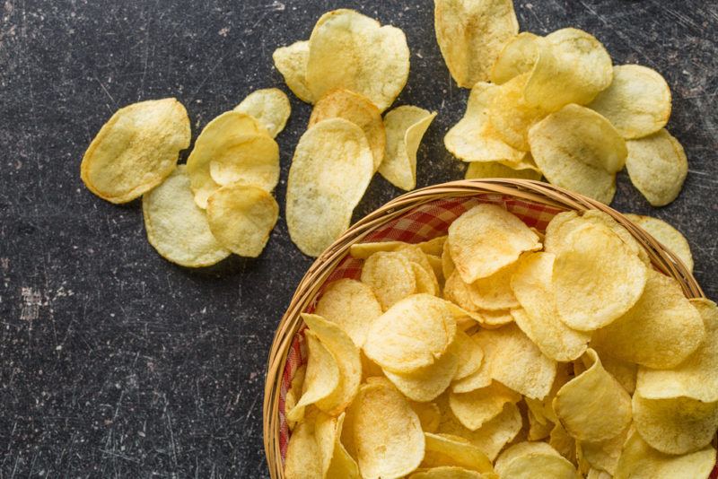 A black table with a basket of chips and some more chips scattered on the table