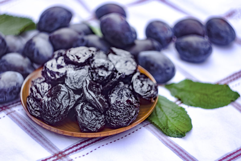 A brown dish with prunes, with plums in the background