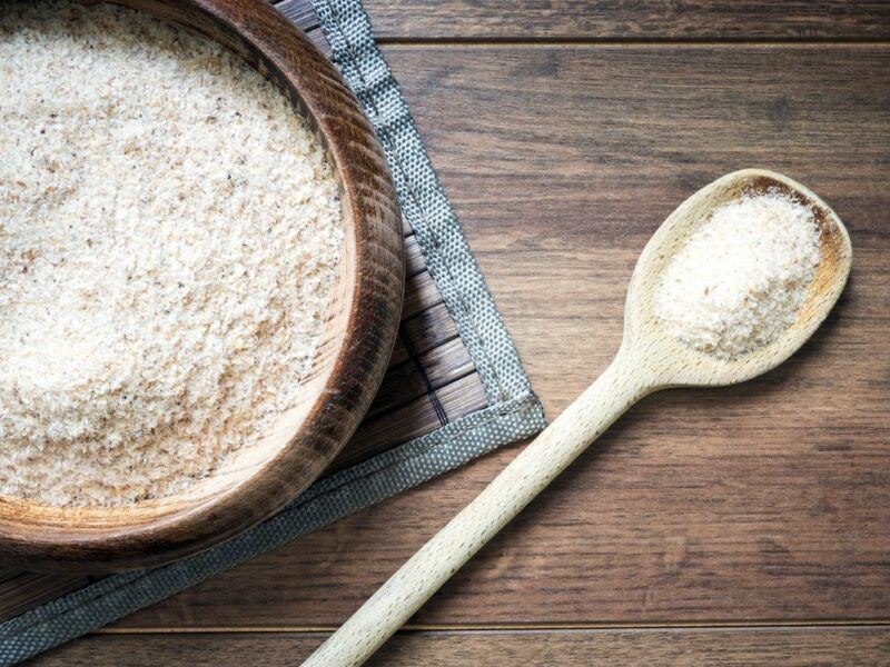 A wooden table with a bowl of psyllium husk powder and a spoon