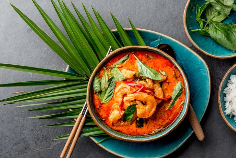 A blue plate with a bowl of Thai red soup on top, with shrimp