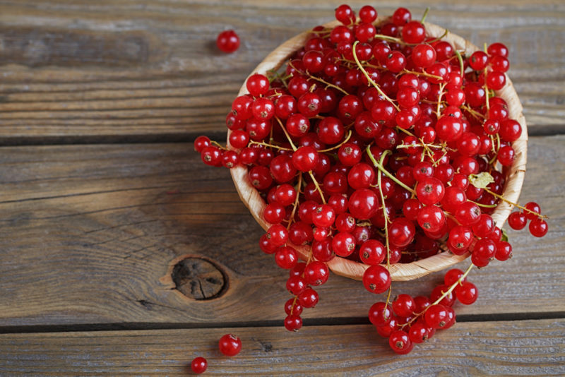 A wooden bowl filled with red currants on a wooden table