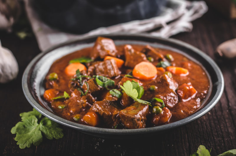A bowl of red meat stew | Food For Net A black bowl containing a rich meat stew
