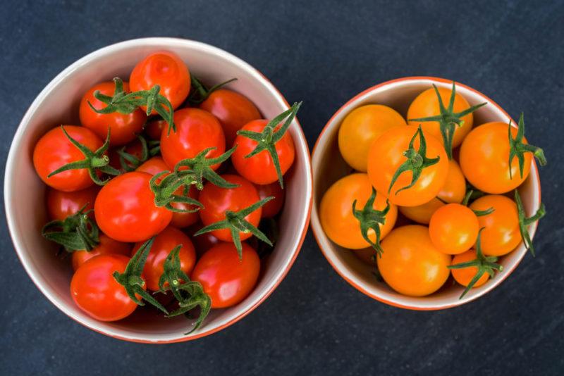 A bowl of red tomatoes and a bowl of yellow ones