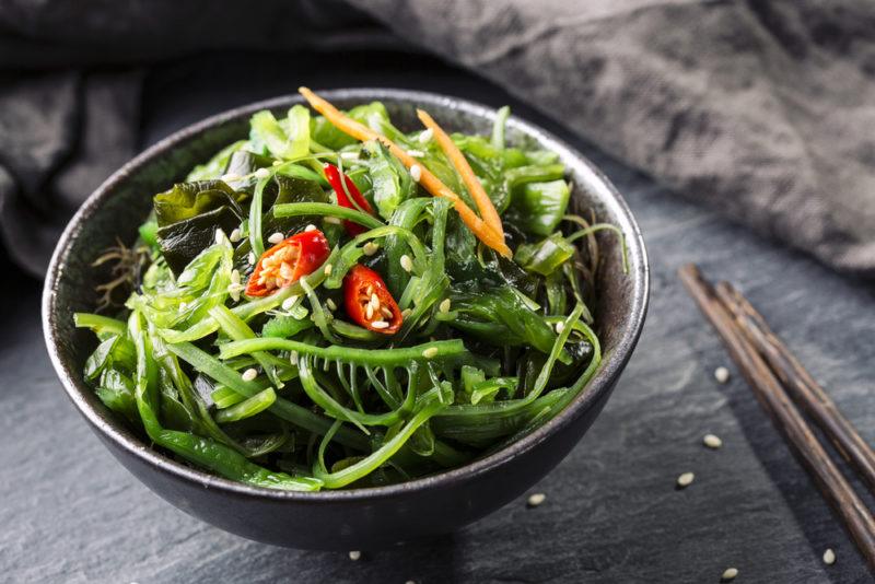 A bowl of seaweed in a dish next to chopsticks