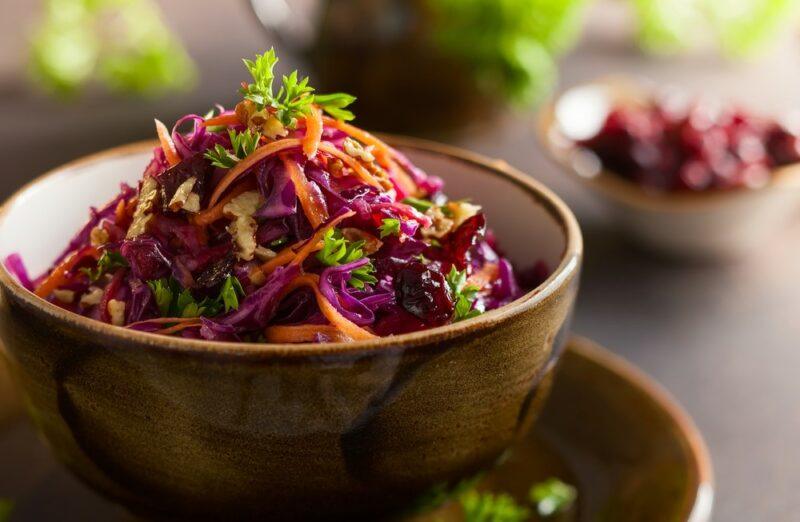 A large dish of a cabbage and carrot salad with ingredients out of focus in the background