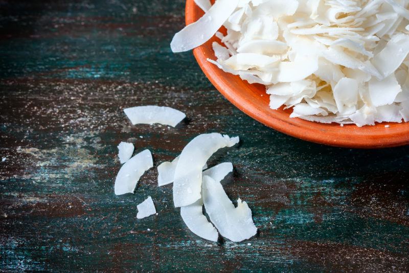 An orange bowl of shredded coconut on a blue wooden table