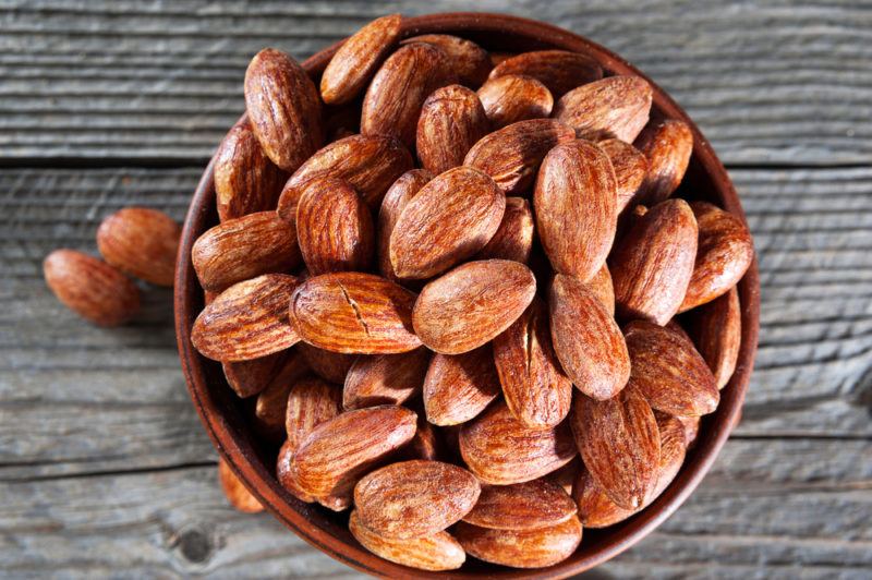 A brown bowl on a wooden table that's filled with smoked almonds