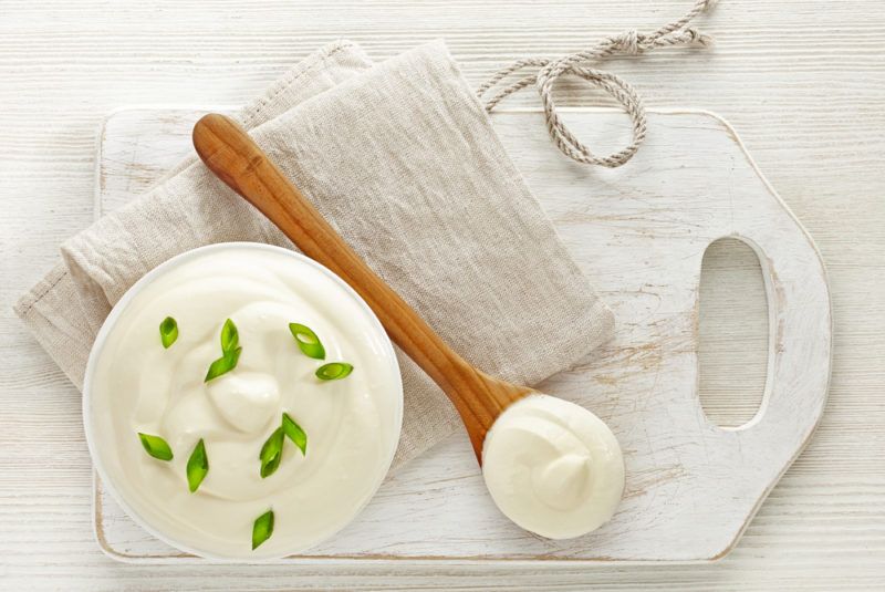 A bowl of sour cream on a white board with a spoon