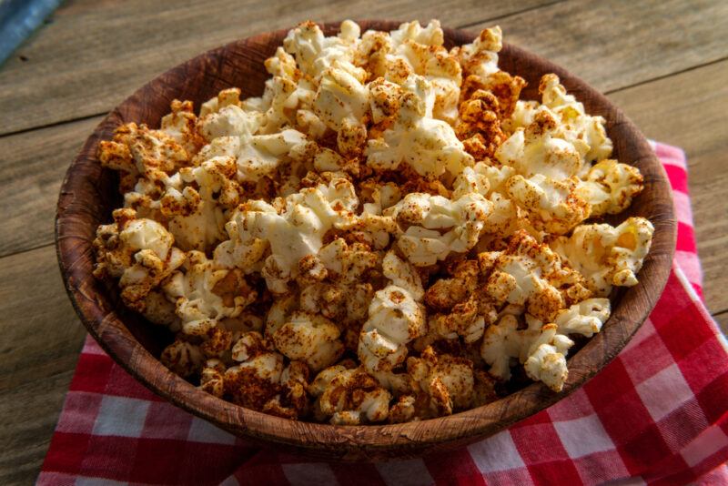 A wooden table with a red and white cloth and a large bowl of spicy herbed popcorn