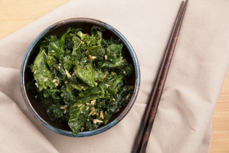 A bowl with stir fried kale next to chopsticks