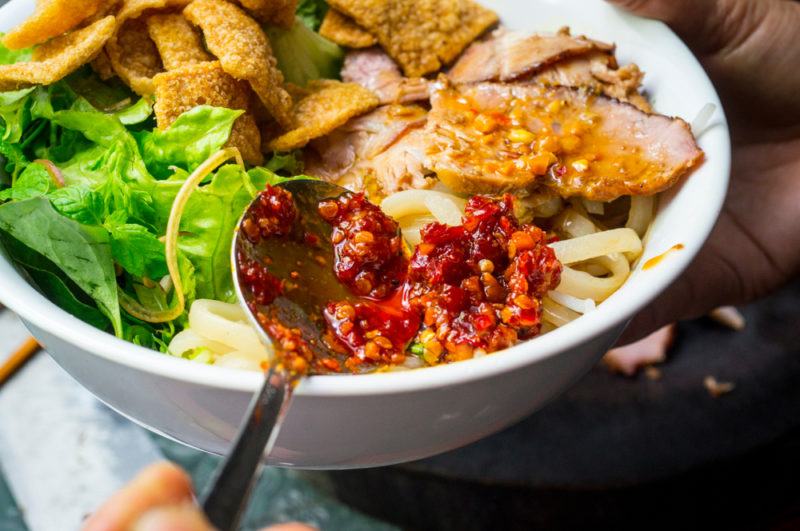 A white bowl with cao lau noodles and a spoon