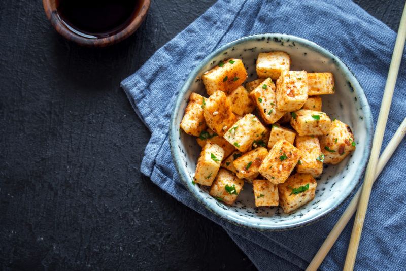 A light colored bowl filled with tofu cubes that have been cooked in sauce