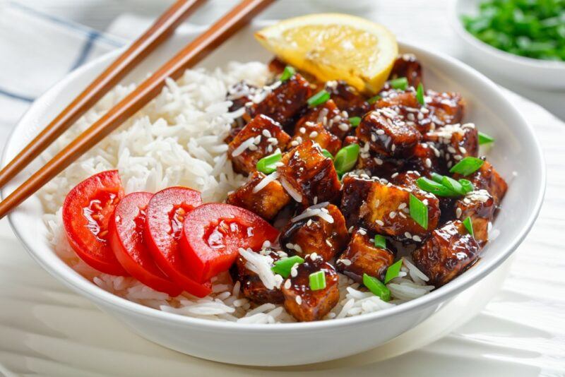 A large white bowl containing white rice, fried tofu, and tomatoes