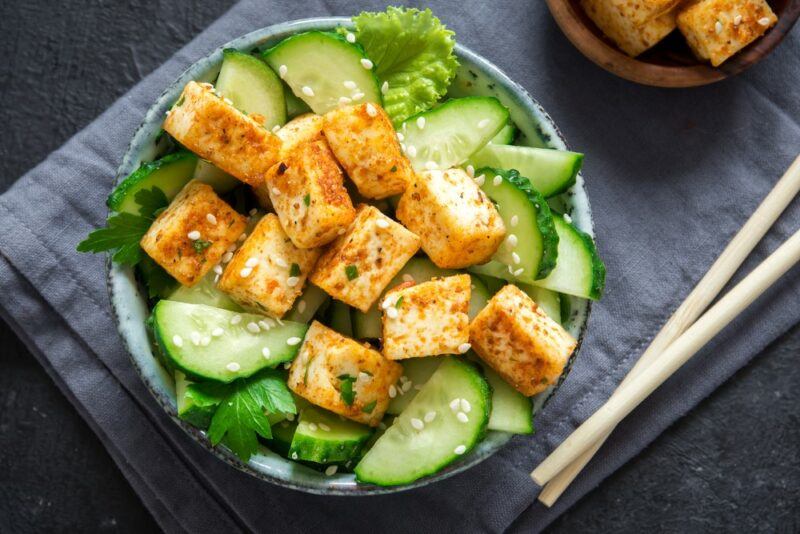 A bowl of salad with cubes of marinated tofu, next to some chopsticks