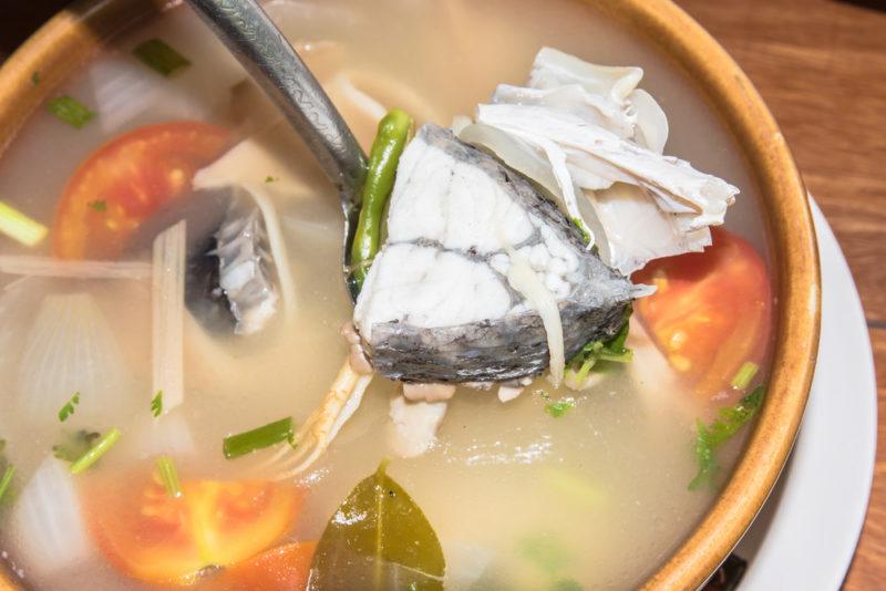 A brown bowl of tom yum soup with fish and clear broth