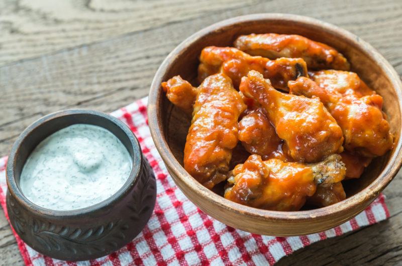 A wooden bowl of chicken wings next to a bowl with blue cheese dip