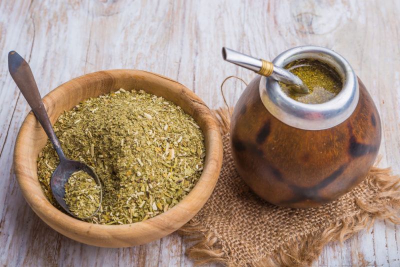 A brown bowl of yerba mate leaves next to a goard