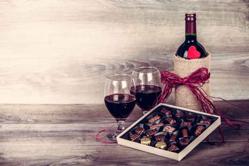 A box of chocolates with a bottle and two glasses of red wine on a wooden table with rustic lighting