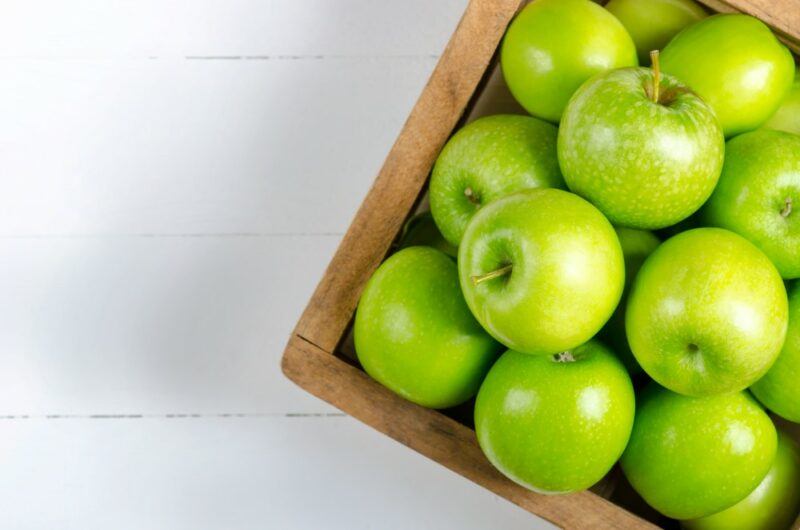 A crate of fresh green apples on a white deck or table