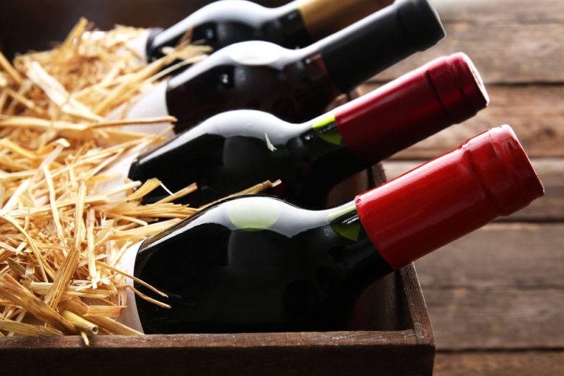 A wooden box with straw and bottles of merlot wines