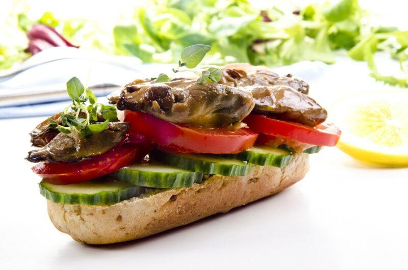 A bread roll that's been cut in half and loaded with cucumbers, tomatoes, and smoked oysters