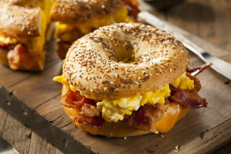 Two fresh breakfast bagels with scrambled eggs and bacon on a wooden board