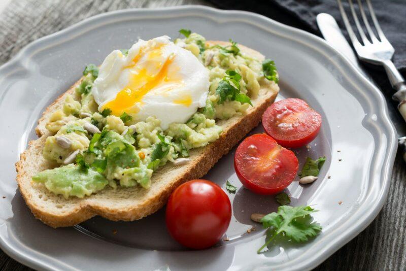 A plate with sourdough for breakfast, which includes mashed avocado and a poached egg, next to some cherry tomatoes