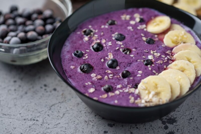 A black bowl containing a purple smoothie bowl with blueberries and bananas