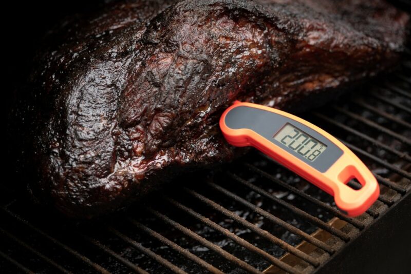 A brisket with a thermometer | Food For Net A piece of brisket on a grill or a smoker, with a thermometer being used to check the temperature