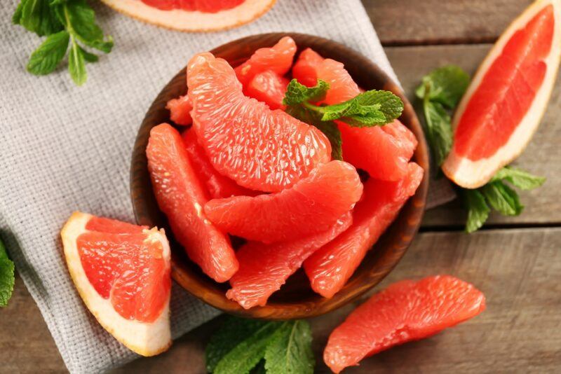 A brown bowl containing peeled grapefruit segments, next to pieces of grapefruit