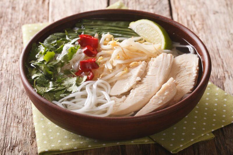 A dark brown bowl containing a rice noodle soup dish